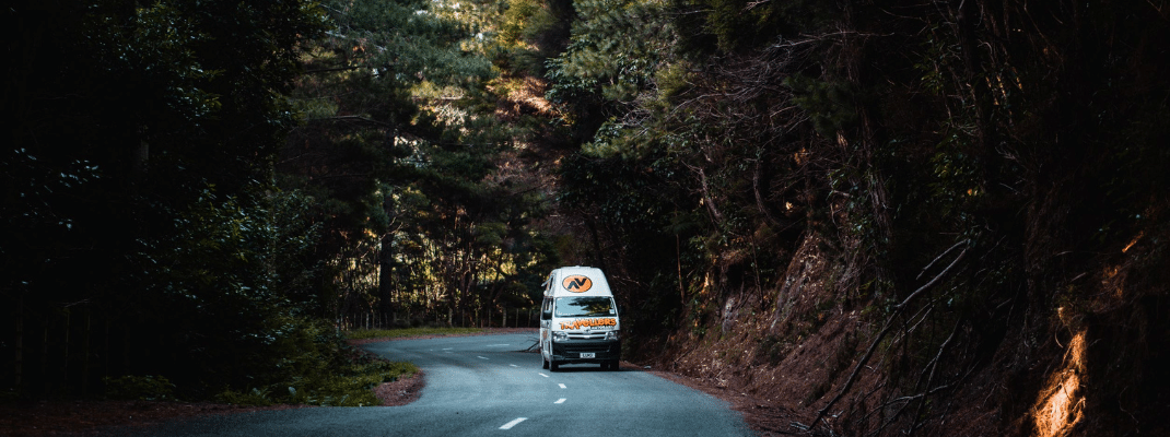 Campervan driving on road through forest, New Zealand